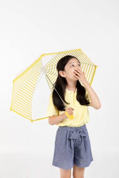cute young Korean girl, rainy season concept in white background studio, surprised by the heavy rain - Foto, afbeelding