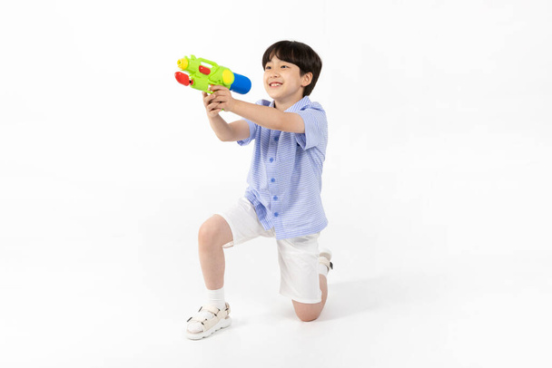 Korean young boy wearing summer blue half sleeve shirt in white background studio_holding a water gun - Photo, image