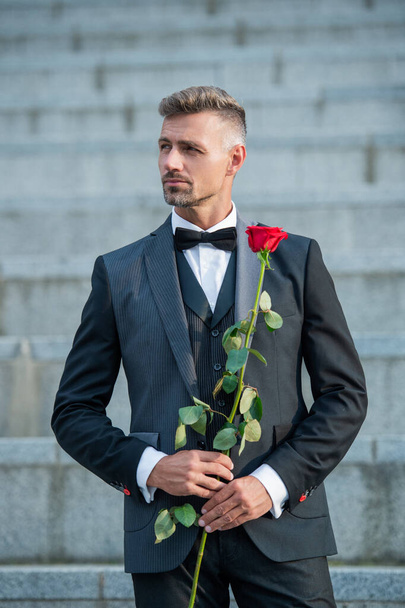 special occasion concept. grizzled man with rose for special occasion. tuxedo man outdoor at special occasion. - Фото, зображення
