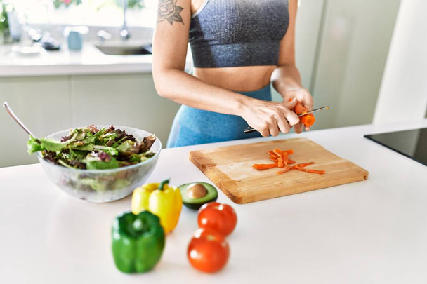 Jonge vrouw snijden wortel voor salade in de keuken - Foto, afbeelding