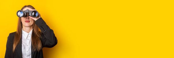 young business woman looking through binoculars on a yellow background. Banner. - Foto, afbeelding