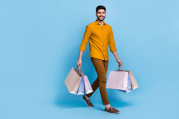Full length photo of positive person walk hands hold packages isolated on blue color background. - Фото, зображення