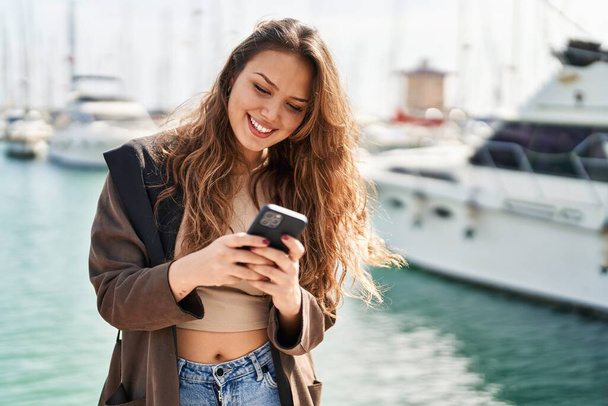 Young beautiful hispanic woman smiling confident using smartphone at seaside - Photo, Image