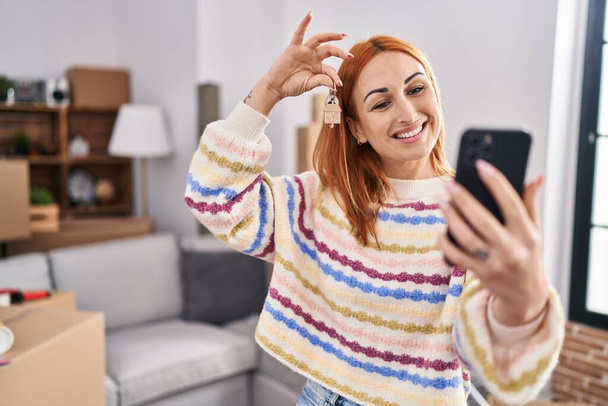 Young caucasian woman having video call holding key at new home - Fotoğraf, Görsel