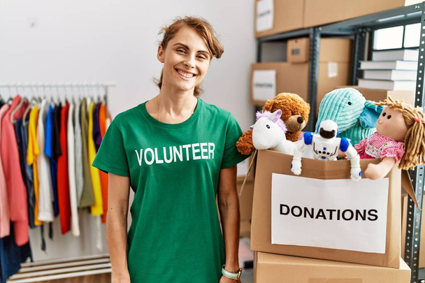 Hermosa mujer caucásica vistiendo camiseta voluntaria en el stand de donaciones con una sonrisa feliz y fresca en la cara. persona afortunada.  - Foto, imagen