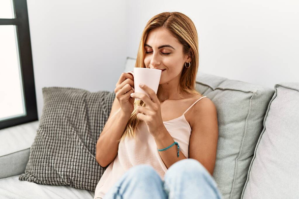 Young caucasian girl smiling happy drinking cup of coffee at home. - Foto, Imagem