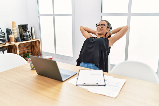 Giovane donna latina sorridente fiducioso rilassato con le mani sulla testa in ufficio - Foto, immagini