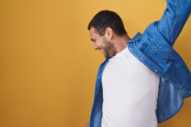 Homem hispânico em pé sobre fundo amarelo dançando feliz e alegre, sorrindo comovente casual e confiante ouvir música  - Foto, Imagem