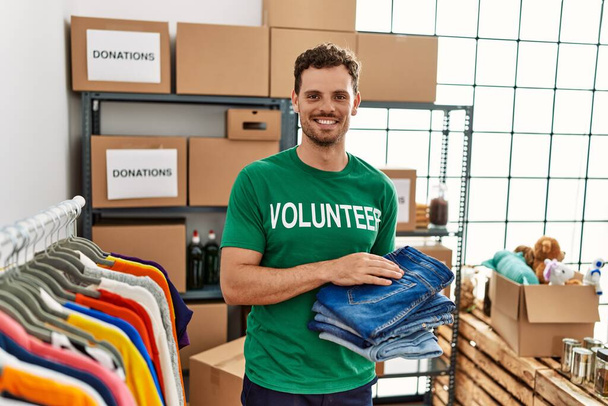 Jonge Spaanse man in vrijwilligersuniform met gevouwen jeans in een liefdadigheidscentrum - Foto, afbeelding