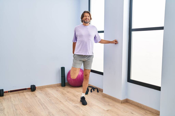 Middle age man smiling confident stretching leg at sport center - Photo, image
