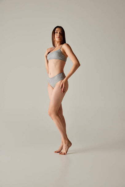 Full-length portrait of young beautiful woman posing in underwear isolated over grey studio background. Slender body shape. Concept of beauty, body and skin care, health, plastic surgery, cosmetics - Φωτογραφία, εικόνα