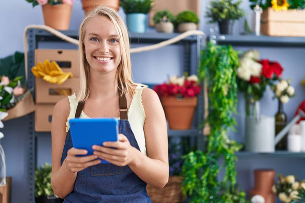 Young blonde woman florist smiling confident using touchpad at florist store - Fotó, kép