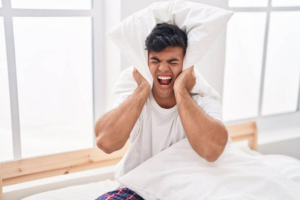 Young hispanic man covering ears for noise at bedroom - Foto, afbeelding