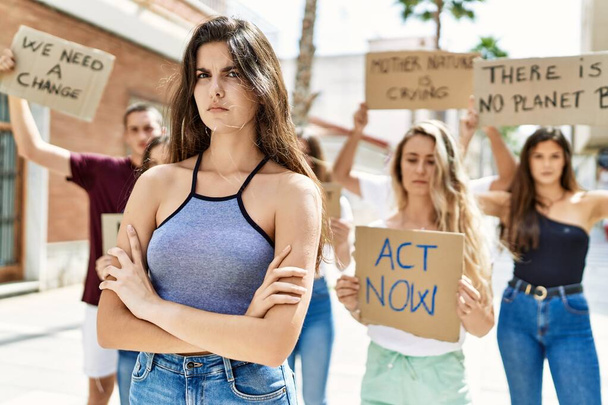 Giovane attivista donna con le braccia incrociate gesto in piedi con un gruppo di manifestanti che tiene banner protestando contro la città. - Foto, immagini