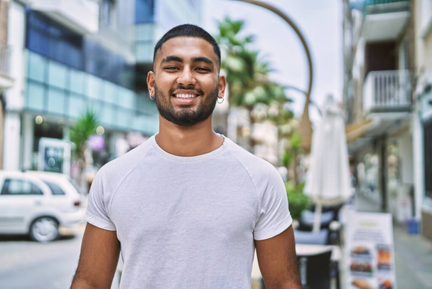 Młody człowiek na Bliskim Wschodzie uśmiecha się szczęśliwy stojąc w mieście. - Zdjęcie, obraz