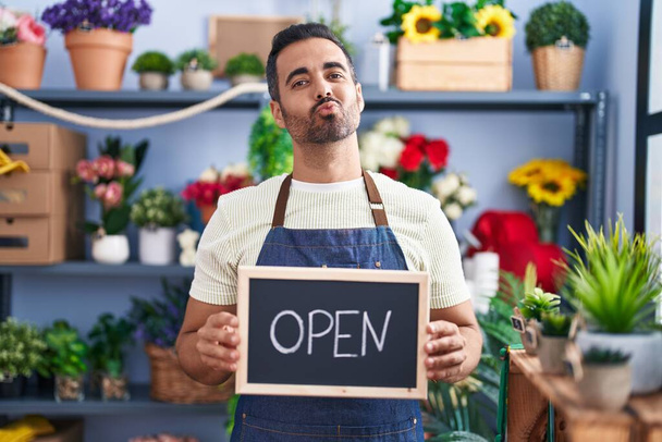 Hispanic man with beard working at florist holding open sign looking at the camera blowing a kiss being lovely and sexy. love expression.  - Фото, зображення