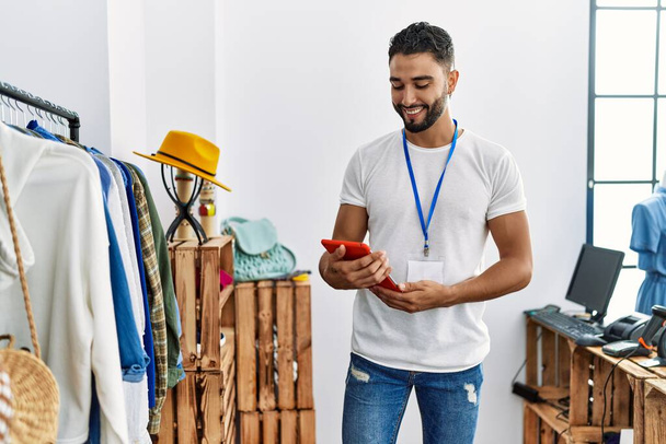 Jeune homme arabe commerçant en utilisant touchpad debout près du porte-vêtements au magasin de vêtements - Photo, image