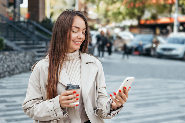 happy young Ukrainian woman looks into her smartphone while sitting on a bench on the street. Girl student reads messages on the phone. Caucasian woman making video calls to relatives - Photo, Image