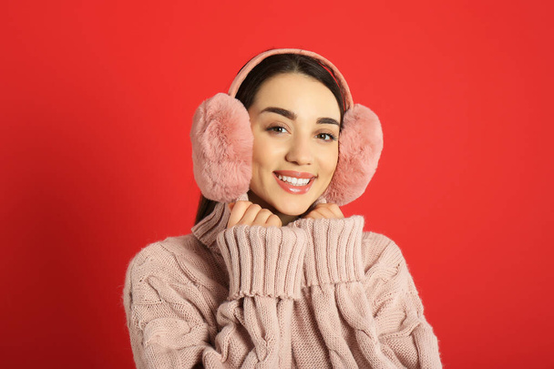 Beautiful young woman wearing earmuffs on red background - 写真・画像