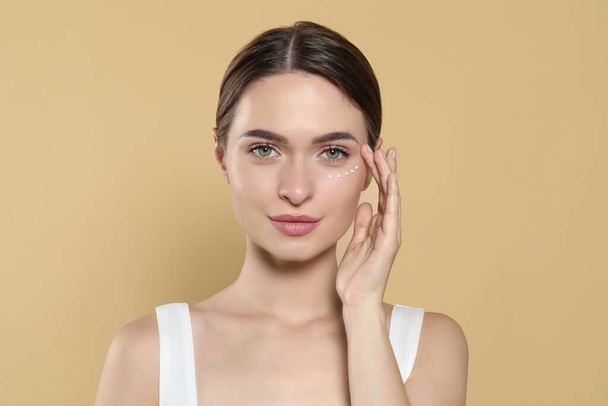 Young woman with cream around eye on beige background - Photo, Image