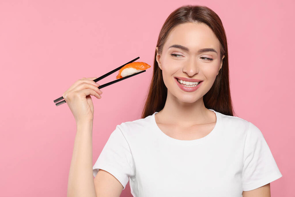 Beautiful young woman holding sushi with chopsticks on pink background - Fotoğraf, Görsel