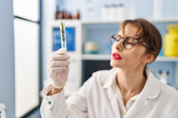 Young caucasian woman wearing scientist uniform holding test tube at laboratory - Фото, изображение