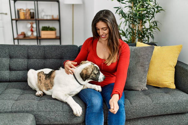 Giovane donna sorridente fiduciosa seduta sul divano con cane a casa - Foto, immagini