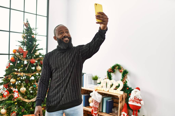 Молодий афроамериканець робить селфі біля смартфону, що стоїть біля христми вдома. - Фото, зображення