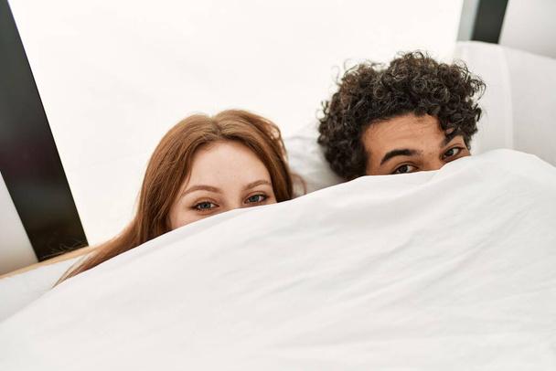 Jeune couple couvrant avec drap de lit couché sur le lit dans la chambre. - Photo, image