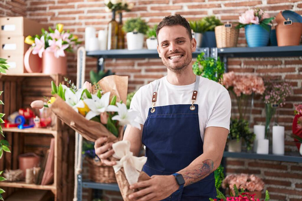 Young hispanic man florist holding bouquet of flowers at florist - Photo, image