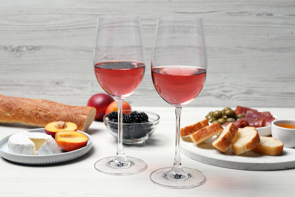 Gläser mit köstlichem Rosenwein und Snacks auf weißem Holztisch - Foto, Bild