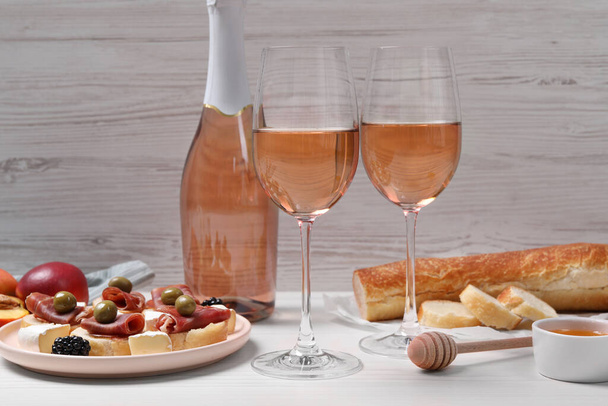 Delicious rose wine and snacks on white wooden table - Foto, Bild