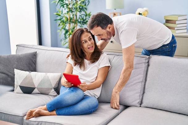 Мужчина и женщина среднего возраста с помощью тачпада сидят дома на диване - Фото, изображение