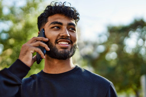 Junger Araber lächelt selbstbewusst und spricht im Park auf dem Smartphone - Foto, Bild