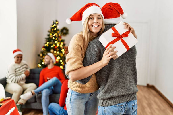 Група молодих людей на різдвяній зустрічі. Пара тримає подарунок і обіймає вдома
. - Фото, зображення