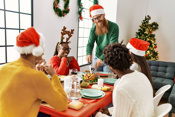Groupe de jeunes souriants heureux d'avoir dîner de Noël, Homme coupe dinde rôtie pour servir à la maison. - Photo, image