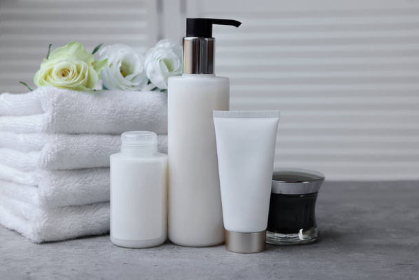 Towels, cosmetic products and flowers on grey table indoors - Fotoğraf, Görsel