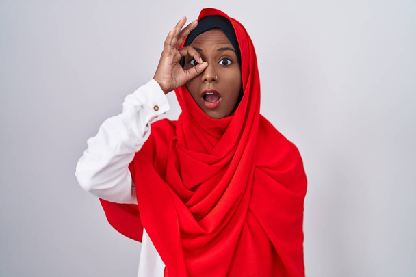 Mladá arabka, oblečená do tradiční islámské hidžábské šály, dělá v pořádku gesto šokované překvapenou tváří, oči hledící skrz prsty. nevěřící výraz.  - Fotografie, Obrázek