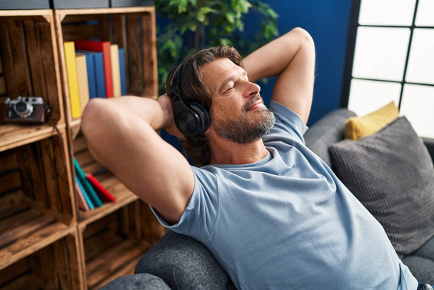 Muž středního věku poslouchající hudbu uvolněný na pohovce doma - Fotografie, Obrázek