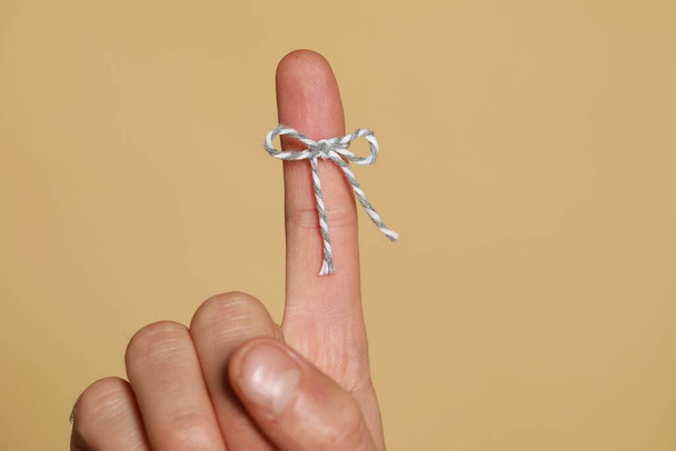 Man showing index finger with tied bow as reminder on beige background, closeup - Foto, Imagen
