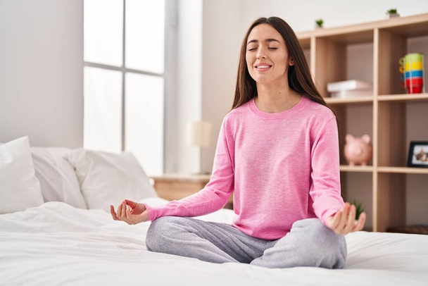Jovem bela mulher hispânica fazendo exercício de ioga sentado na cama no quarto - Foto, Imagem