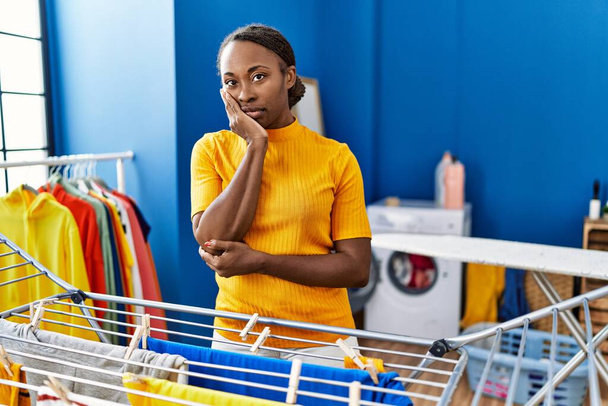 Afrikaanse vrouw opknoping kleren op waslijn denken kijken moe en verveeld met depressie problemen met gekruiste armen.  - Foto, afbeelding