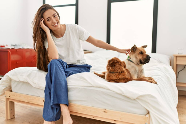 Young hispanic woman smiling confident sitting with dogs on bed at bedroom - Foto, immagini