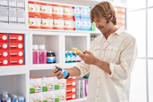 Fiatal férfi ügyfél, hogy fotó gyógyszer palack okostelefon a gyógyszertárban - Fotó, kép