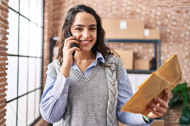 Genç İspanyol kadın ecommerce iş işçisi ofisteki akıllı telefondan konuşuyor. - Fotoğraf, Görsel