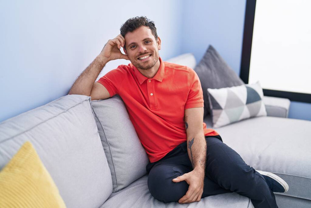 Joven hombre hispano sonriendo confiado sentado en el sofá en casa - Foto, Imagen