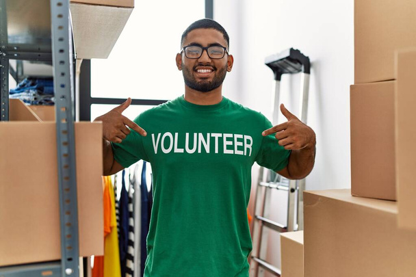 Jonge Arabier man wijzend met vingers naar vrijwilliger uniform op liefdadigheidscentrum - Foto, afbeelding