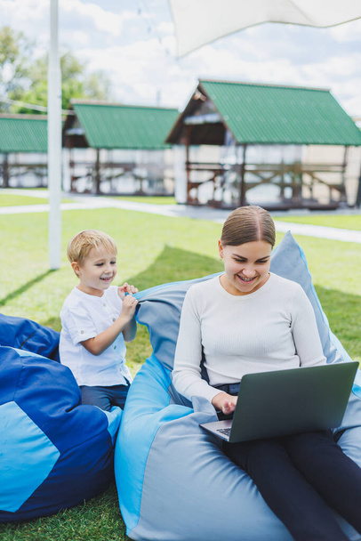 Cute young mother and son looking at laptop. Happy family, mother and son are resting in the park. A woman on maternity leave - Valokuva, kuva
