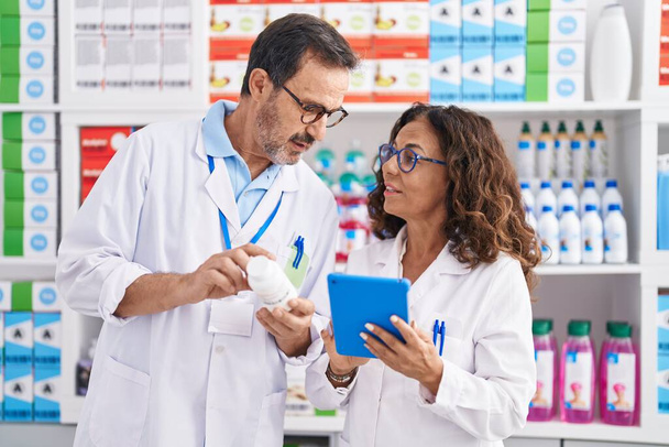 Мужчина и женщина фармацевты с помощью тачпада держат бутылку с таблетками в аптеке - Фото, изображение
