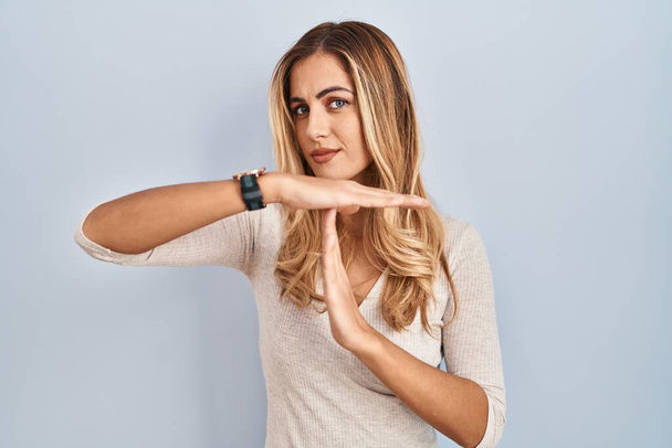 Young blonde woman standing over isolated background doing time out gesture with hands, frustrated and serious face  - Photo, Image
